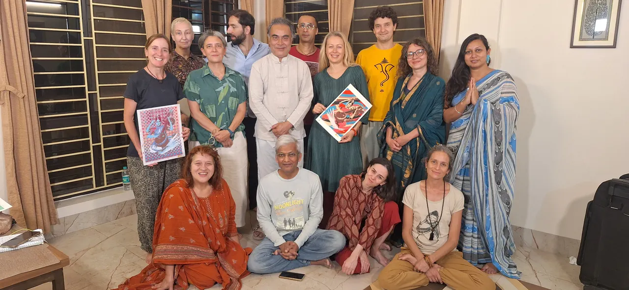 Group portrait of participants standing and sitting together indoors, two of them holding colourful prints