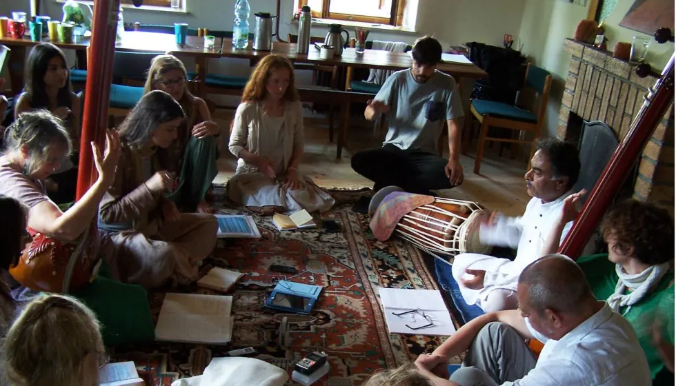 Indoor Dhrupad vocal training session with tanpura and pakhawaj, students seated around the teacher